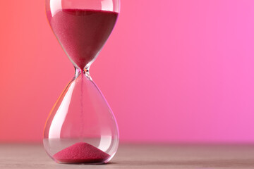 Hourglass with flowing pink sand on table against color background. Space for text