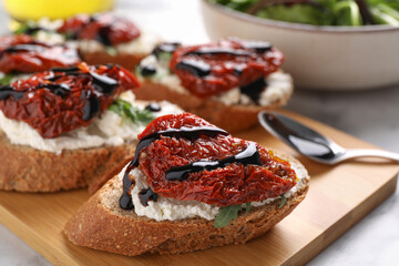 Delicious bruschettas with sun-dried tomatoes, cream cheese and balsamic vinegar on light table, closeup