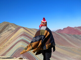 Rainbow mountain or seven colors mountain view in the red valley in the andes. Poncho and chullo are the two main dressing peruvian clothes in the picture.