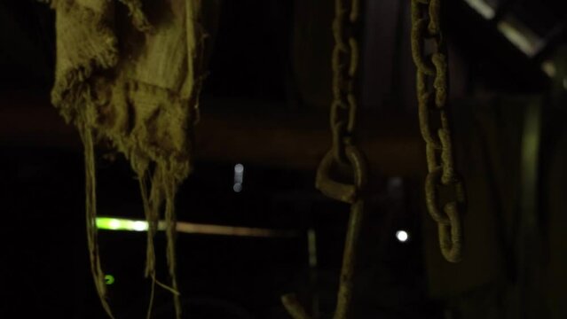 Rusty chains hang from the ceiling and dangle in an abandoned basement, a metal chain and rusty hook move in an old barn