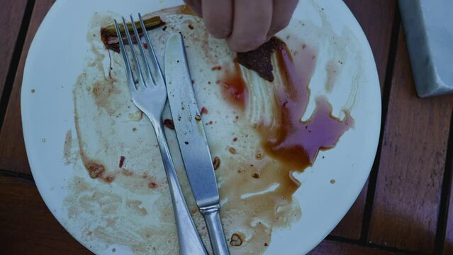 Savoring the Last of Hand Dips Bread into Remaining Sauce on Empty Plate