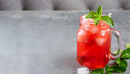 Iced fruit tea or cold watermelon drink in clear glass with mint leaf. Refreshing summer drink. Grey background, copy space.