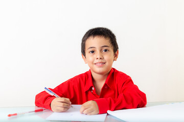 .A cute boy in red shirt sitting and writing doing homework..The cute boy wearing a red shirt..emotion through the face..Studio portrait, concept health with white background.  .funny face..