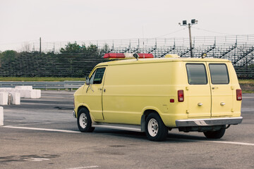 vue sur une fourgonnette jaune à l'arrêt sur une piste de course avec des gradins en arrière plan lors d'une journée ennuagée