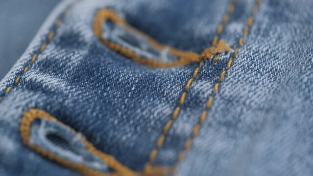 rotation of fabric of blue jeans in closeup details. button holes on blue denim jeans. denim texture, abstract background. clothing concept and tailoring.