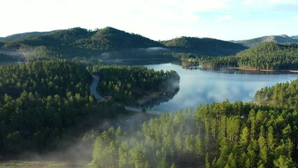 A scenic road runs adjacent to a pristine lake at the foot of the Black Hills