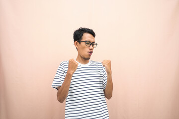 Asian man in glasses wearing casual striped t-shirt, happy gesture getting surprise. Isolated beige background.