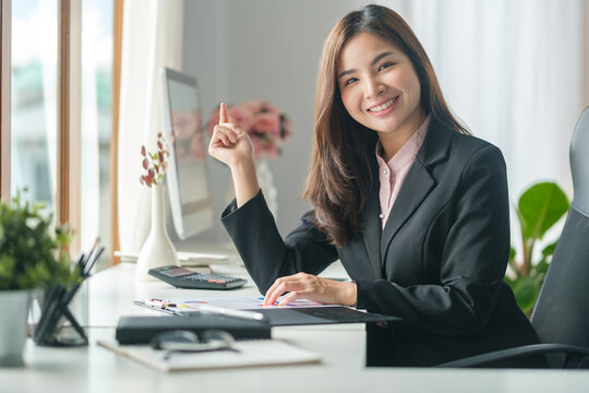 Gorgeous Millennial Businesswoman In Black Suit Sitting At Working Desk And Smiling To Camera.