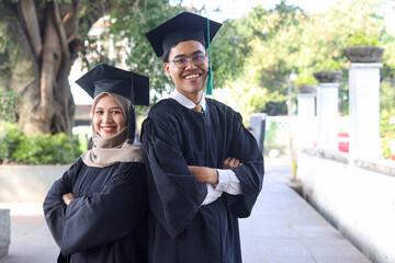 Picture of two friends in mortar board and graduation gown standing back to back with crossed hands...