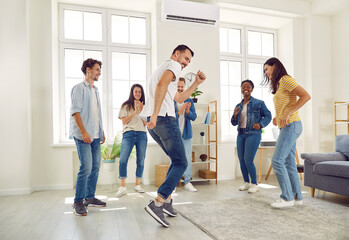 Six cheerful best friends are dancing and fooling around listening to their favorite track at home party. Multiracial men and women laughing and having fun standing in circle in living room.