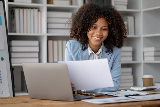 American woman sitting working in a startup company, american businesswoman working in the office, she is looking at financial documents and sales data to summarize before meeting with executives.