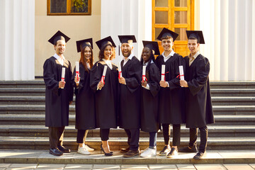 Group of cheerful students on graduation day. Seven happy joyful multiracial graduates in black...