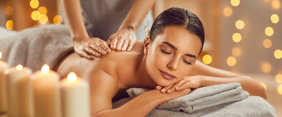 Beautiful young woman enjoying massage in spa salon. Relaxed brunette girl lying on massage bed with closed eyes during spa treatment procedure. Beauty treatment, skin care, wellbeing