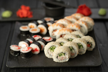 Sushi set with a variety of delicious rolls on a black plate on a dark wooden background, top view
