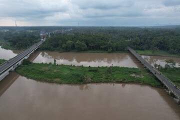 Aerial view of the long bridge over the brown watery river. the river delta is overgrown with green...