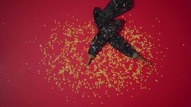 Mexican chili peppers tossed on a red surface with chili seeds