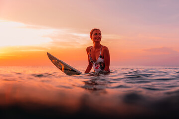 Surfer lady with surfboard in ocean on warm sunset or sunrise.