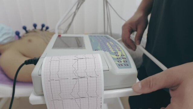 the doctor makes a cardiogram to the patient who is lying on the medical couch. the result is printed on paper with a conclusion