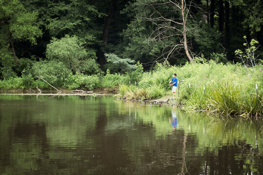 Boy casting fishing line into lake on a summer day.