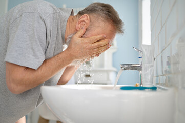 Senior man washing face at sink in home bathroom
