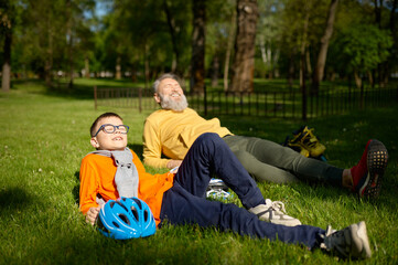 Happy positive smiling grandpa and grandson rest on green grass meadow in park