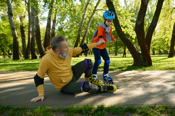 Little boy teaching old grandfather roller skating in park