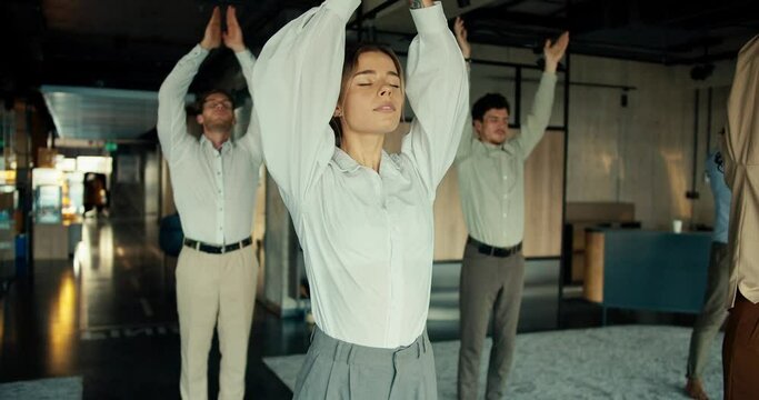 A blonde business girl in a white shirt is doing yoga with her colleagues in the office. Take a break from work to maintain spiritual strength and stability