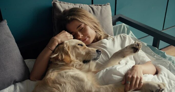 Close-up shot: a blonde girl sleeps in bed with her light-colored dog in the morning. Happy pet owner