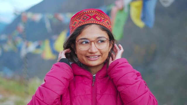 Teenager girl wearing red jacket and Himachali topi (Himachali traditional cap), A North Indian young woman standing outdoor with beautiful mountains view in background at Lahaul, Himachal