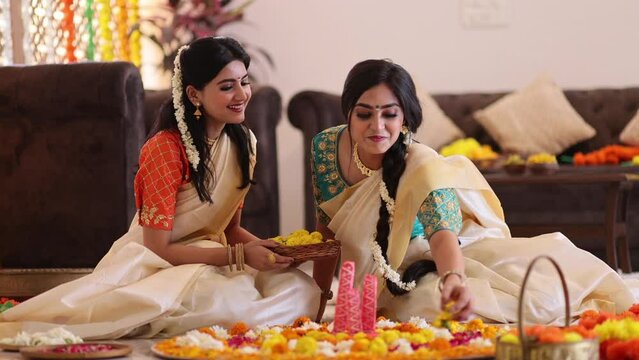 South Indian Women in white saree decorating house with flowers to celebrate Onam	