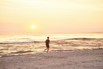 Fototapeta na wymiar Silhouette of a sportsman running near the ocean shore at sunset.