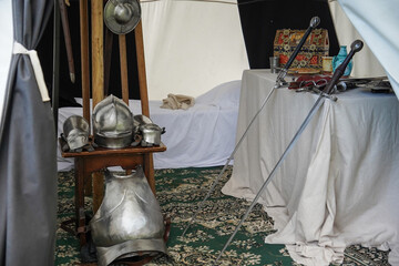 Close up of medieval knight equipment in old sleeping tent. Metal helmet, shield, sword and clothes. Traditional knights weapons at middle age theme festival    