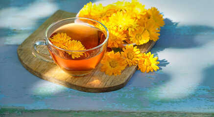 glass cup with herbal tea and fresh yellow-orange calendula flowers close up on rustic wooden...
