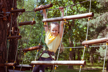 Child in a forest adventure park made of ropes. Children's outdoor climbing entertainment center. Playground for children and sports with a cableway. Sports suspended rope trainer.