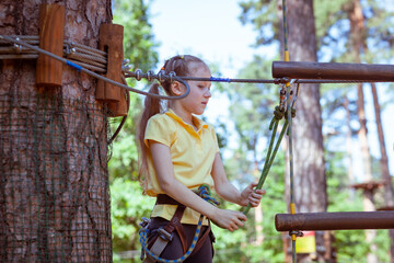 Child in a forest adventure park made of ropes. Children's outdoor climbing entertainment center. Playground for children and sports with a cableway. Sports suspended rope trainer.