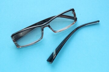 Old broken eyeglasses with damaged legs on blue background. Poor eyesight. Reuse and repair concept. Idea of health. Failure optic eyewear. Breakage of vision correction glasses. Close up, flat lay