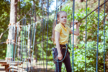 Child in a forest adventure park made of ropes. Children's outdoor climbing entertainment center. Playground for children and sports with a cableway. Sports suspended rope trainer.