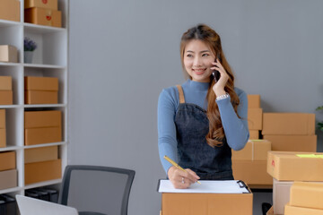 Happy Asian woman owner talking on the phone with customers, taking orders and preparing delivery.