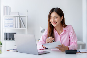 Smiling young happy Asian businesswoman working with laptop and documents in office. Accountant or beautiful asian female worker working happily in the office.