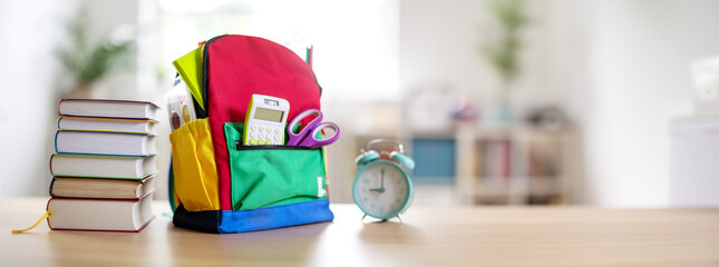 Colourful backpack with stationery standing on the table indoors.