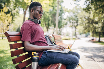 Obraz premium Young man sitting in the park and using laptop
