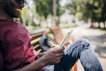 Young man sitting in the park relaxing in the nature and using digital tablet