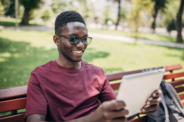 Fototapeta premium Young man sitting in the park relaxing in the nature and using digital tablet