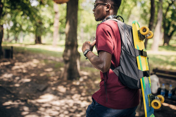 Young man walking in the park and carrying skateboard