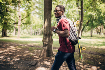 Young man walking in the park and carrying skateboard