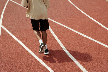 Fototapeta premium Low part of active schoolboy in sportswear running down track on sunny morning while training or taking part in race or competition