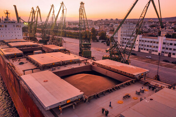 Aerial of wheat loading to bulker ship cargo hold at sea grain elevator in sea port at sunset....