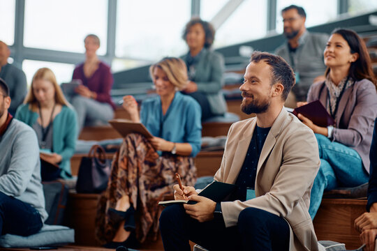 Happy entrepreneur taking notes while attending business seminar in conference hall.