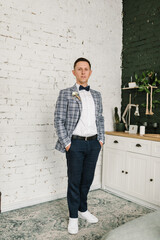 Groom. Handsome happy groom near brick wall in room or studio. Portrait of man. Groom is waiting for bride, first meeting. Luxury wedding day. Fashion photo. Man preparing for wedding. Closeup.