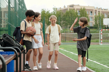 Obraz premium Group of happy youthful classmates in activewear enjoying stroll on stadium while one of them explaining something to his friends